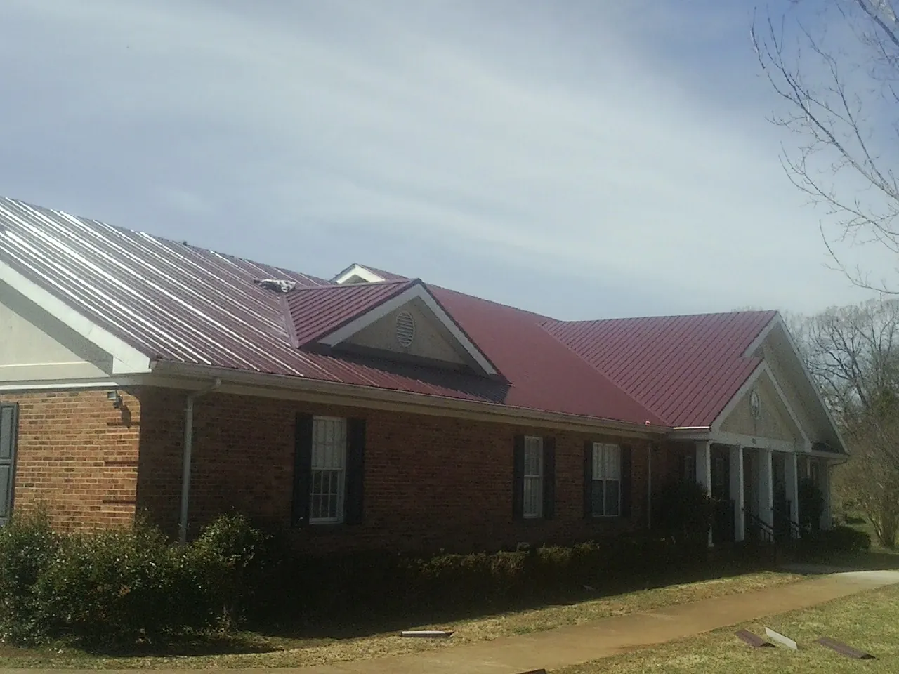 Red metal roof with gabled entries on a long brick building, from a Hail Damage Roof Repair job in Addison