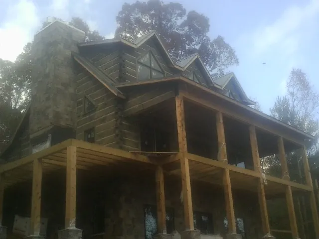 Stone chimney and dormers on a large log home with a timber porch in Addison
